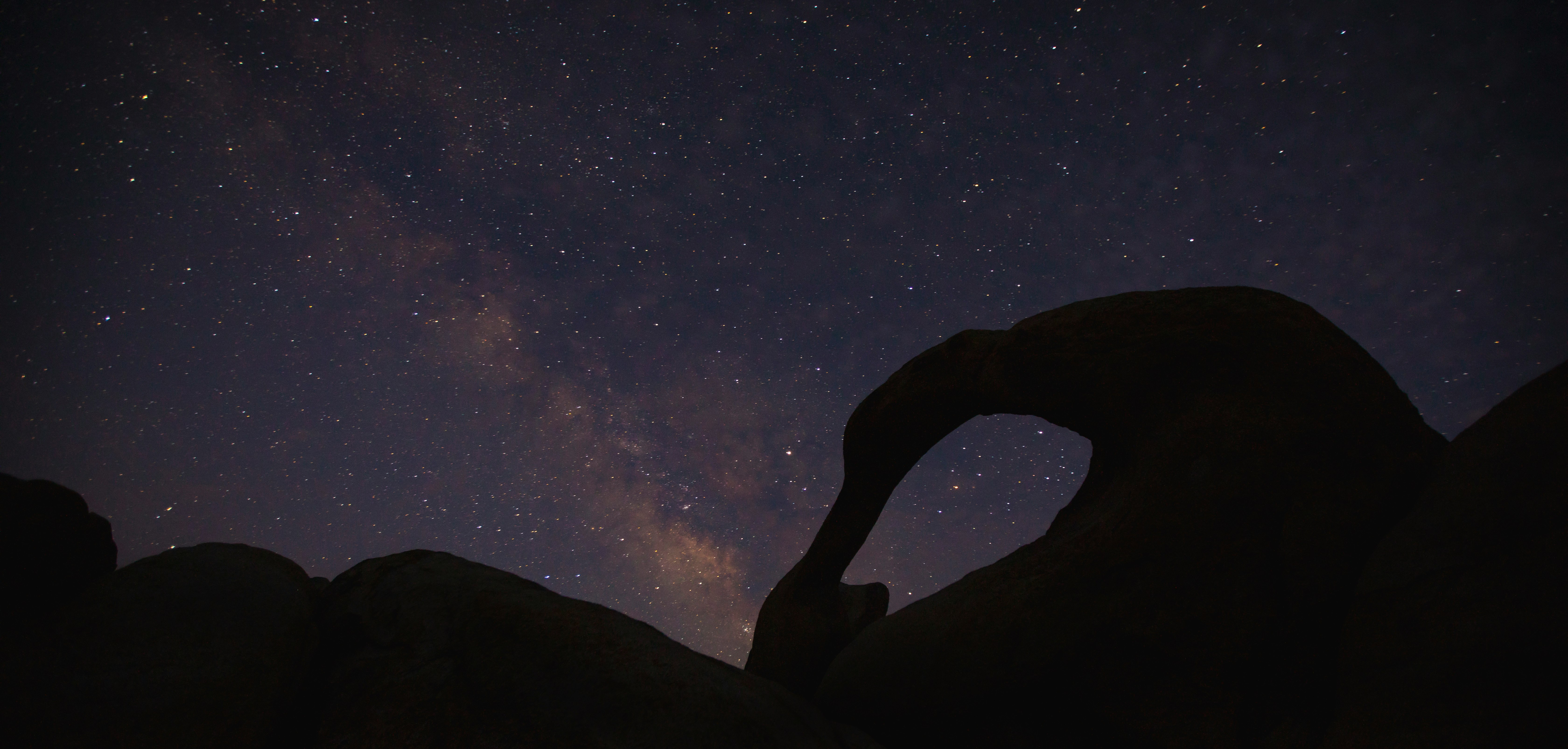 silhouette of person standing on rock formation under starry night